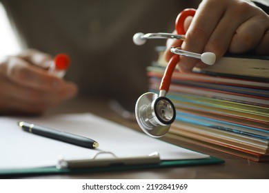 Male Doctor In White Lab Coat Reading Text Book, Search Information And Working On Laptop Computer With  Medical Stethoscope On The Desk In Room At Clinic. Medical Knowledge And Education Concept.