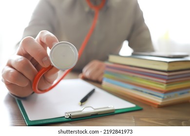 Male Doctor In White Lab Coat Reading Text Book, Search Information And Working On Laptop Computer With  Medical Stethoscope On The Desk In Room At Clinic. Medical Knowledge And Education Concept.