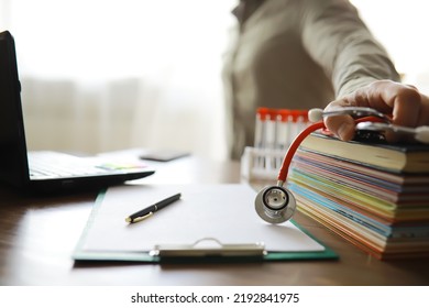 Male Doctor In White Lab Coat Reading Text Book, Search Information And Working On Laptop Computer With  Medical Stethoscope On The Desk In Room At Clinic. Medical Knowledge And Education Concept.