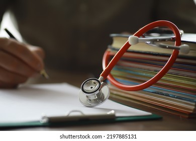 Male Doctor In White Lab Coat Reading Text Book, Search Information And Working On Laptop Computer With  Medical Stethoscope On The Desk In Room At Clinic. Medical Knowledge And Education Concept.