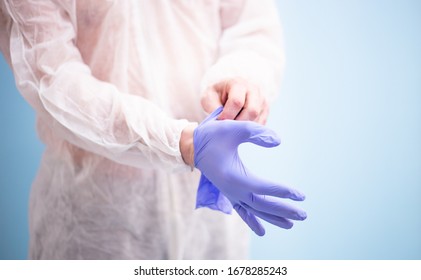 Male doctor in white virus protective suit puts on medical rubber gloves for work in blue. - Shutterstock ID 1678285243
