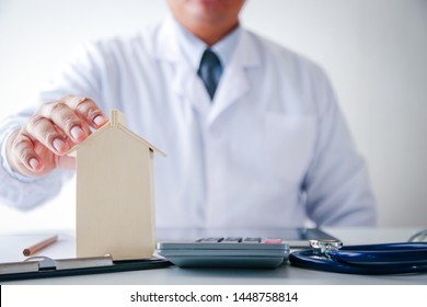 The Male Doctor Wore A White Dress, Holding A Toy House On The Table. Real Estate Care Concept