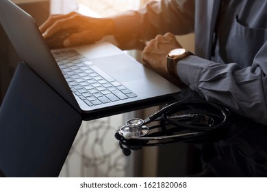 Male Doctor Working On Laptop Computer, Using Wireless Mouse With Medical Stethoscope On The Desk In Medical Room At Clinic Or Hospital. Electronic Health Record System (EHRs), Telehealth Concept.