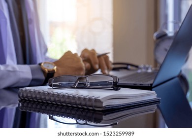 Male Doctor Working And Typing On Laptop Computer Keyboard With Notebook And Eye Glasses On The Desk At Medical Office .Teleconference, Telehealth, Online Medical, Medic Tech, Emr, Ehr Concept. 