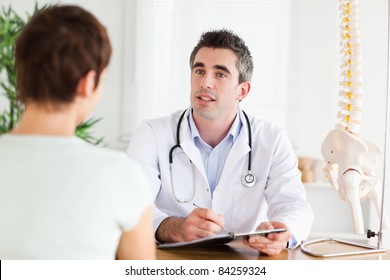 Male Doctor writing something down while patient is talking in a room