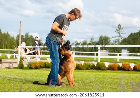 A male dog handler, owner of a young German shepherd dog, trains his dog on a training field.