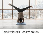 A male doing a headstand yoga exercises at the gym room overlooking a Swiss Alps.