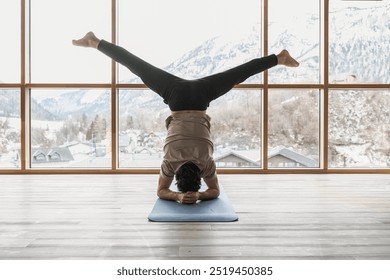 A male doing a headstand yoga exercises at the gym room overlooking a Swiss Alps. - Powered by Shutterstock