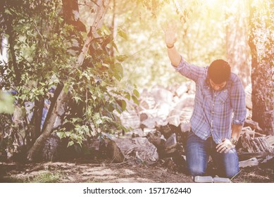 A male down on his knees on the ground with his hand towards the sky with the sun shining in the background