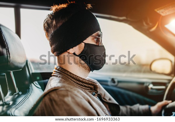 male driver in a\
black medical mask and sunglasses rides behind the wheel on a sunny\
day. pandemic concept.