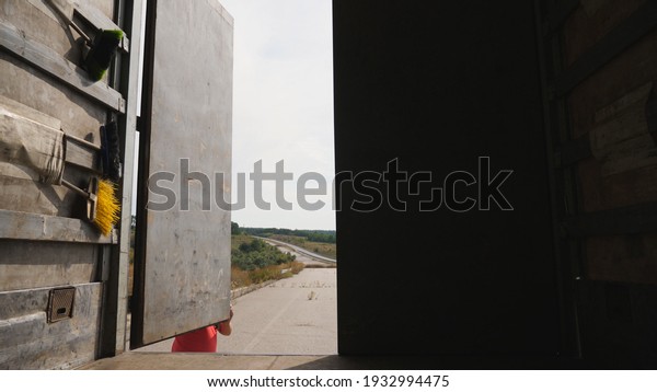 Male driver closing rear door of truck at\
countryside. Lorry parked at country road. Car is ready to deliver\
the goods. View from inside of semi-truck. Logistics concept. Close\
up Slow motion.