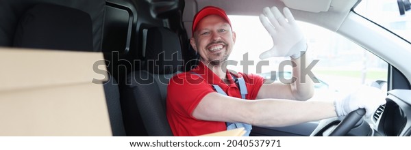 Male driver courier in cab of car waving his\
hand in greeting