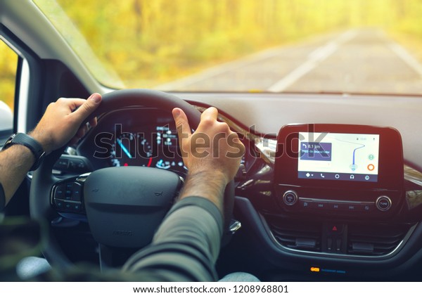 Male driver with hands on the steering wheel\
driving on road in autumn warm\
colors
