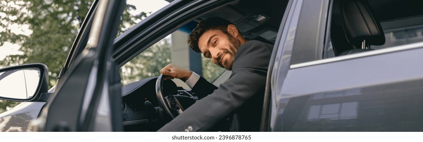 Male driver looking at camera while sitting in driver seat with opened door. High quality photo