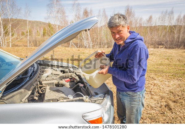 Male\
driver pours washer fluid into the tank of a\
car.
