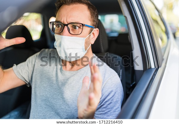 Male driver with protective face mask under stress\
inside car.