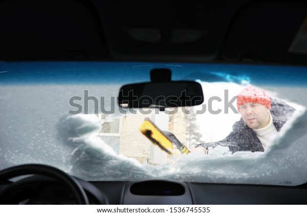 A male driver\
is standing in front of a car. The owner cleans the car from snow\
in winter. Car after a\
snowfall.