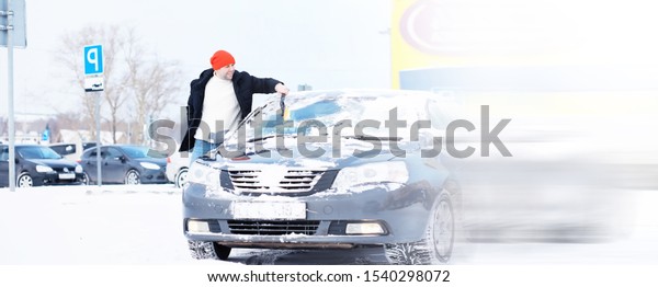 A male driver is\
standing in front of a car. The owner cleans the car from snow in\
winter. Car after snowfall.