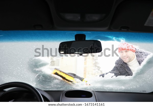 A male driver\
is standing in front of a car. The owner cleans the car from snow\
in winter. Car after a\
snowfall.