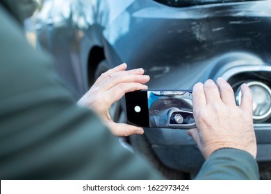 Male Driver Taking Photo Of Damaged Car After Accident For Insurance Claim On Mobile Phone