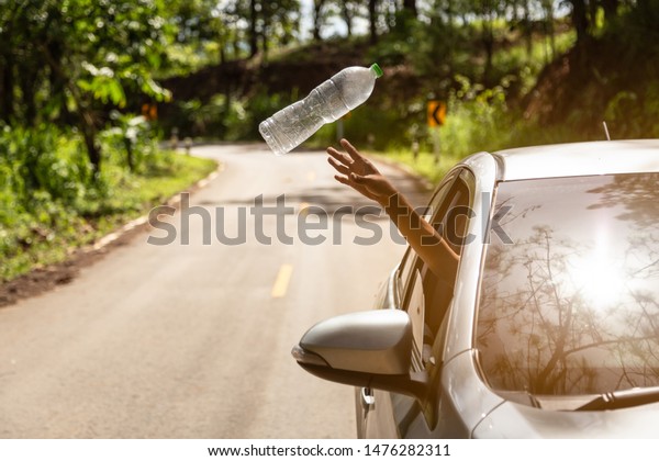 Male driver throwing away plastic bottle from car\
window on the road,man’s hand or arm throwing garbage while driving\
on valley road in green nature,environmental protection,global\
warming concept