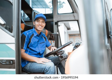 A male driver in uniform smiles at the camera while sitting behind the steering wheel on the bus