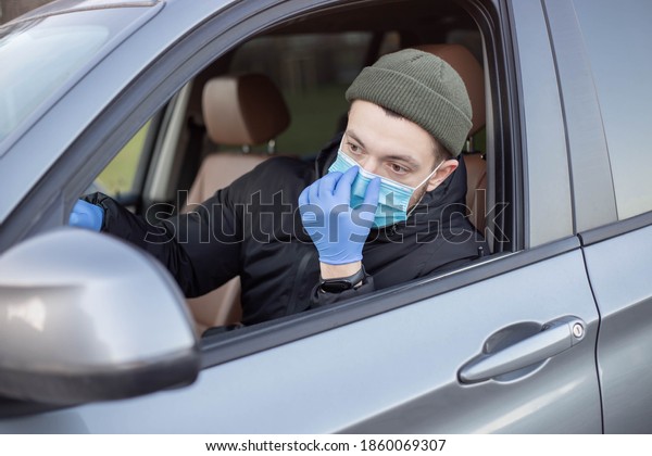 Male driver wearing mask in car during coronavirus\
outbreak.White bearded man wearing protective mask to avoid the\
infection of virus and polluted air spreading deseases inside of\
his car. 