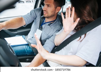 Male driving instructor holds steering wheel and try to avoid a car accident. Young woman raised her hands. Safety driving a car concept. Fastened seat belts. Obtaining a driver's license concept