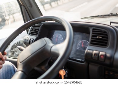 Male Driving A Truck And Holding Steering Wheel Of Truck During The Movement In The Road. Image With Selective Focus On The Wheel, Dashboard With Speedometer And Tachometer, Blurred Windshield