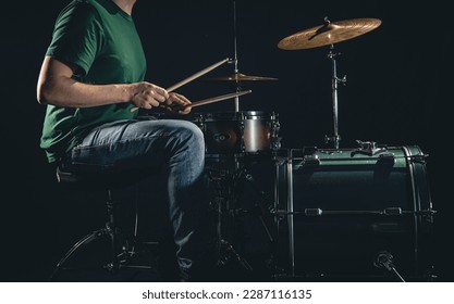 A male drummer plays a drum kit on a black background, a professional musician plays drums.