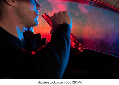 Male Drunk Driver With Beer Bottle In Car On The Background Of Police Car Lighting.