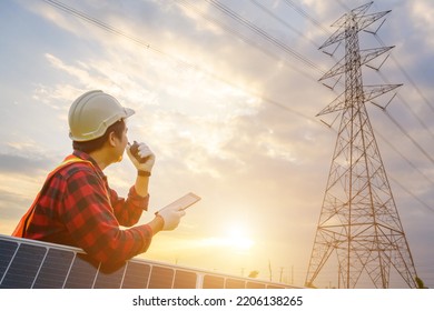 A Male Electrical Engineer Looks At A Power Station And Solar Photovoltaic Panels To See The Power Generation Planning Work At A High Voltage Pole.