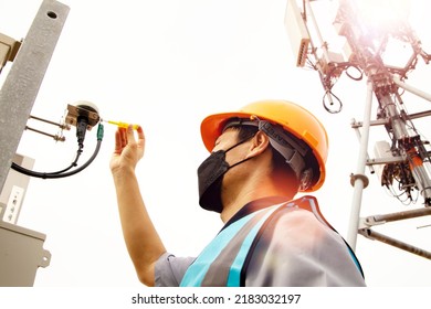 Male Electrical Engineer Wearing Helmet And Mask Uses Screwdriver Check The Safety Of The Sensor Terminals Outside The Telecommunication  Tower Control Cabinet Check The Leakage Current And Safety.