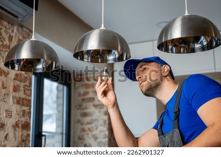 Male electrician changes the light bulbs in the lamp. A young man in overalls performs technical work on electrification of premises