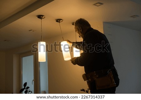 A male electrician changes the light bulbs in the ceiling light. men's household duties. care of electrical appliances at home