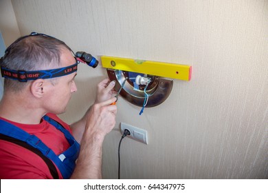 Male electrician connects the lamp on the wall