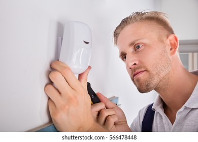 Male Electrician Installing Security System Door Sensor On Wall