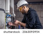 A male electrician works in a switchboard with an electrical connecting cable.