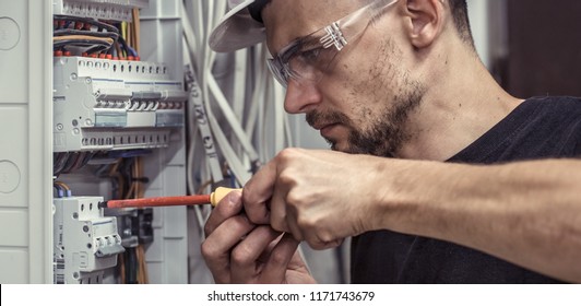 a male electrician works in a switchboard with an electrical connecting cable, connects the equipment with tools, the concept of complex work, space for text