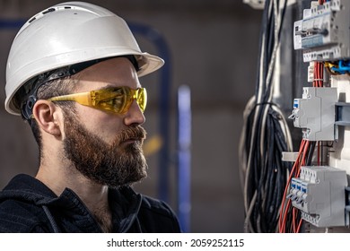 A male electrician works in a switchboard with an electrical connecting cable. - Shutterstock ID 2059252115