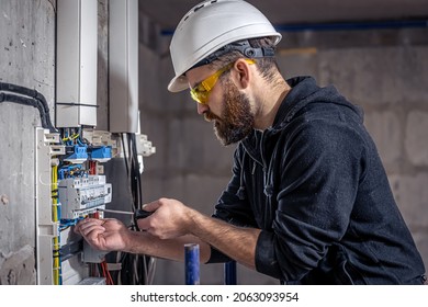A male electrician works in switchboard and an electrical connecting cable 