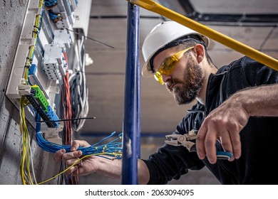 A male electrician works in switchboard and an electrical connecting cable 