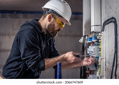 A male electrician works in a switchboard with an electrical connecting cable. - Shutterstock ID 2066747609