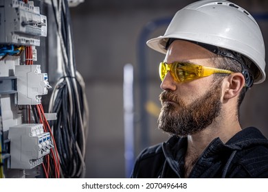A male electrician works in a switchboard with an electrical connecting cable. - Shutterstock ID 2070496448
