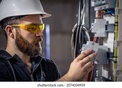 A male electrician works in a switchboard with an electrical connecting cable. - Shutterstock ID 2074334959