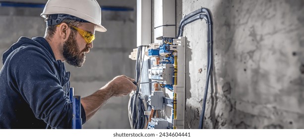 A male electrician works in a switchboard with an electrical connecting cable. - Powered by Shutterstock