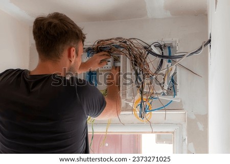 A male electrician works in a switchboard with an electrical connecting cable. Electrical panel in the apartment on a white wall. Fuse box