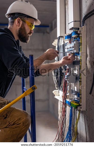 A male electrician works in a
switchboard with an electrical connecting
cable.