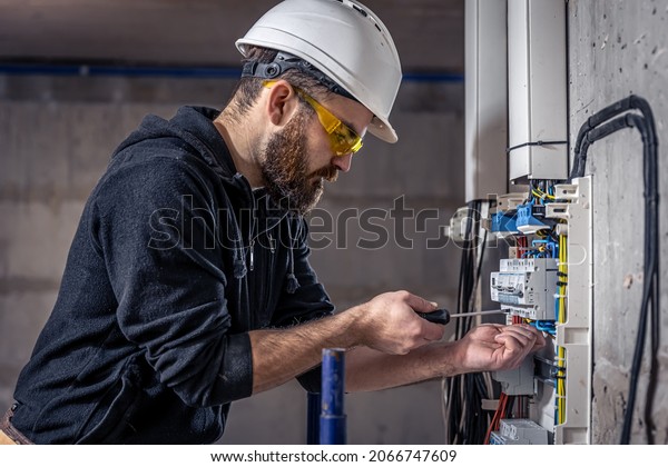 A male electrician works in a\
switchboard with an electrical connecting\
cable.
