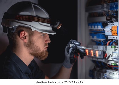 A male electrician works in a switchboard in overalls against the backdrop of emergency lighting.